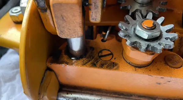 Zbliżenie na mechanizm zębatkowy pomarańczowego lewarka z widocznymi śladami oleju.
