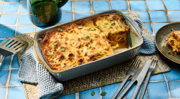 Herzhafte Moussaka mit Zucchini, goldbraun gebacken, wartet darauf, serviert zu werden. Ein Stück ist bereits auf einem Teller angerichtet.