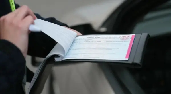 Policjant wypisuje mandat karny za kolizję. Dokument jest otwarty, widać jego numer.