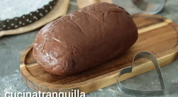 Pâte sablée au chocolat prête à être façonnée. Un emporte-pièce en forme de cœur est à proximité, suggérant de délicieuses créations.