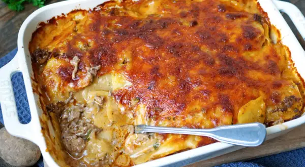Herzhafter kartoffelauflauf mit Hackfleisch, überbacken mit goldbraunem Käse. Eine Gabel steckt in der dampfenden Schüssel.