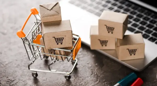 Miniaturowy wózek sklepowy z paczkami na laptopie. To jest właśnie retail – zakupy online w pigułce.