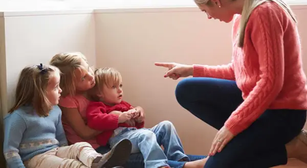 Kvinna pekar på barn som sitter på golvet. Kanske ett svårt samarbetssamtal med narcissist.
