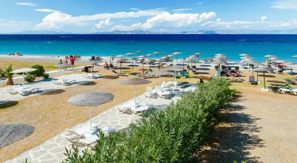 Słoneczna plaża Faliraki by Sun Palace z leżakami i parasolami. Turkusowe morze i góry w tle.
