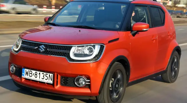 Pomarańczowy Suzuki Ignis z czarnym dachem pędzi po drodze. Kierowca w środku.