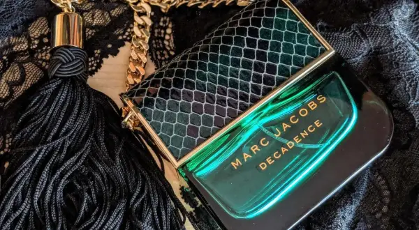 Flakon perfum Marc Jacobs Decadence w zielonym, wężowym wzorze, z czarnym frędzlem i złotym łańcuszkiem, emanuje luksusem.