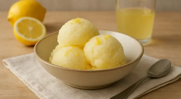 En skål med tre kulor **limoncello sorbet**, garnerad med citronskal. Bredvid finns en halv citron, en hel citron och ett glas med gul vätska.