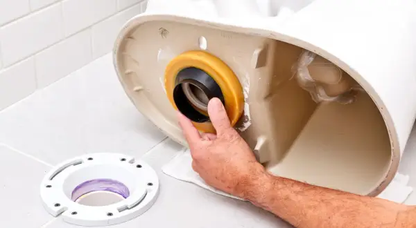 Hand installing a wax ring onto the base of a toilet, preventing a toilet leaking at base.