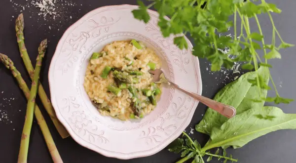 Un crémeux risotto asperges, garni de morceaux d'asperges fraîches, servi dans une assiette rose, avec des asperges crues à côté.
