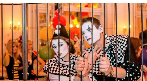 Zwei Clowns hinter Gittern, bereit für den Dresden Karneval. Bunte Ballons und Lichter im Hintergrund.