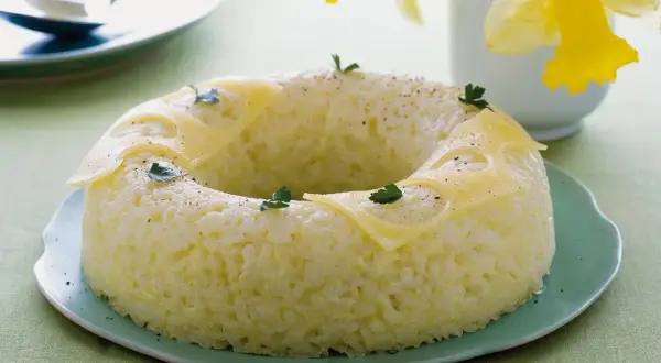 Sformato di riso a ciambella, decorato con fette di formaggio e prezzemolo, su un piatto verde.