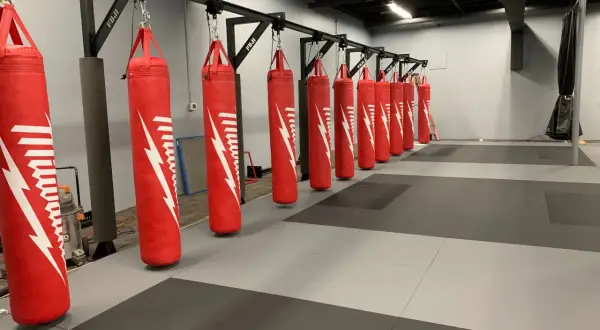A row of red punching bags hangs from a metal rack, demonstrating how to hang a punching bag for optimal training.