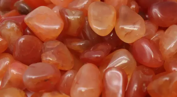 Tanti sassolini levigati di agata marrone, con sfumature arancioni e rosse, noti per le loro proprietà energizzanti.
