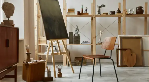 An art studio aesthetic with a canvas on an easel, wooden furniture, sculptures, and art supplies.