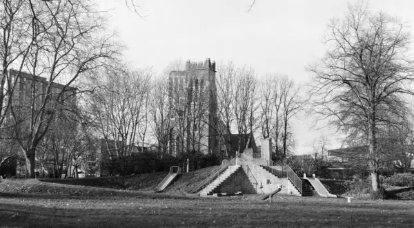 A playground with slides and stairs, captured on Ilford Pan 400 film, stands amidst bare trees with a brick tower in the background.