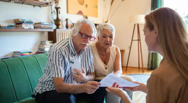Un couple âgé discute avec une conseillère des modalités de calcul du paiement d'une maison de retraite par les descendants.
