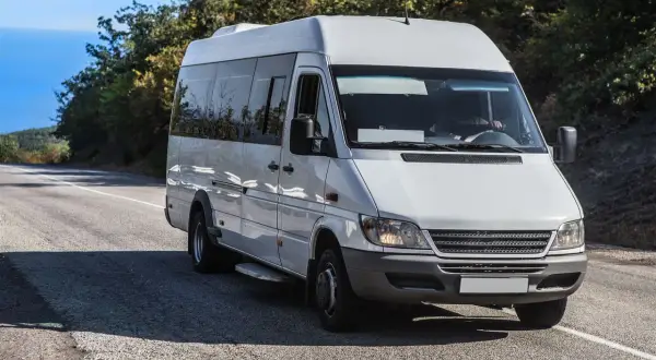 Weißer Kleinbus von Polen nach Deutschland fährt auf einer Straße durch eine hügelige Landschaft.