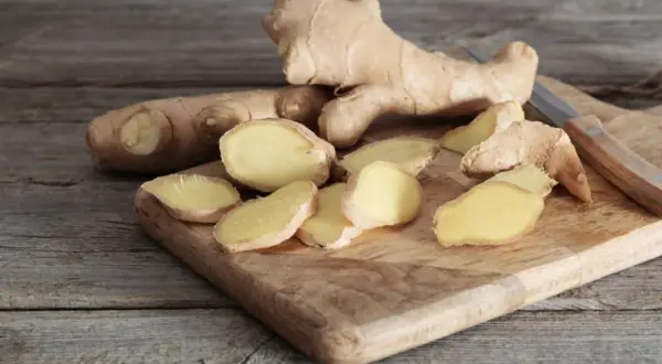 Frischer Ingwer, teils in Scheiben geschnitten, liegt auf einem Holzbrett. Der Unterschied zwischen ganzen Wurzeln und den Scheiben ist deutlich zu erkennen.