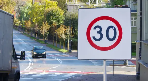 Znak strefa 30 na tle jesiennej ulicy z przejściem dla pieszych i samochodem.