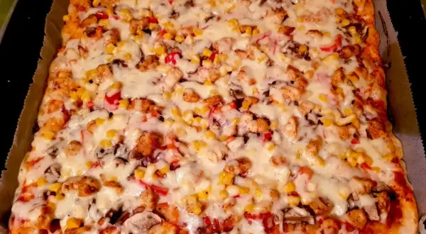 Pyszna pizza domowa na blachę z kurczakiem, kukurydzą i pieczarkami, obficie posypana serem. Idealna na rodzinny obiad.