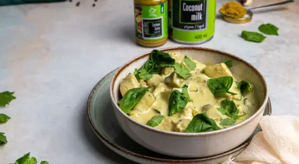 Miseczka zielonego curry z kurczakiem i szpinakiem, obok puszka mleka kokosowego i słoiczek pasty curry.