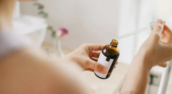 Kobieta aplikuje serum z pipetką na dłoń. Bezpieczny niacynamid w ciąży to klucz do promiennej cery.