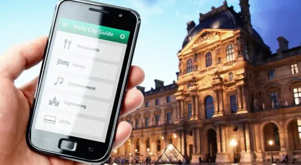 Smartfon z przewodnikiem po Paryżu w dłoni, w tle Luwr. Odkrywaj kody Francji!
