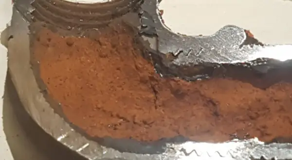 Sezione di tubo metallico con incrostazioni marroni che mostrano come evitare la formazione di calcare nelle tubazioni.