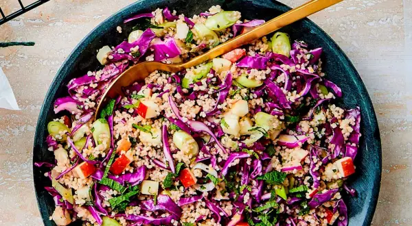 En färgstark couscous sallad med rödkål, äpple och färska örter. En gyllene sked vilar i den fräscha rätten.