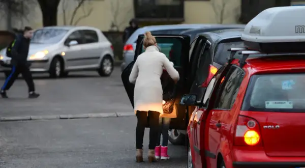 Kobieta z dzieckiem wsiada do samochodu, obok stoją inne auta.