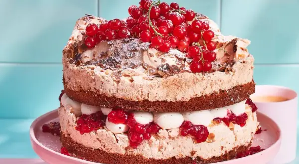 Ein zweistöckiger Johannisbeer Baiser Kuchen mit Schokoladenböden, Sahne und roten Johannisbeeren.