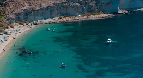 Gente disfrutando del sol y el mar en la playa de San Pedro. Barcos y motos acuáticas navegan en aguas cristalinas.