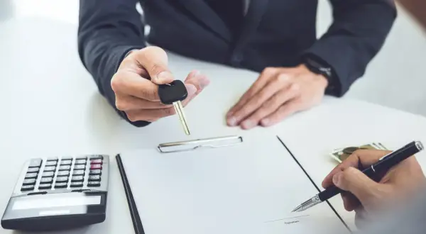 Przekazanie kluczyków do samochodu po podpisaniu umowy leasingu finansowego. Obok kalkulator i pieniądze.