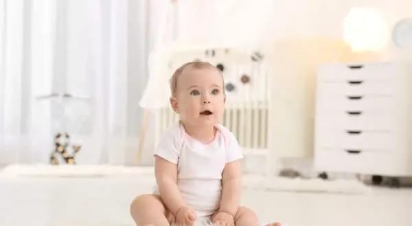 Urocze dziecko z niebieskimi oczami, kiedy dziecko siada na miękkim dywanie w pokoju dziecięcym.