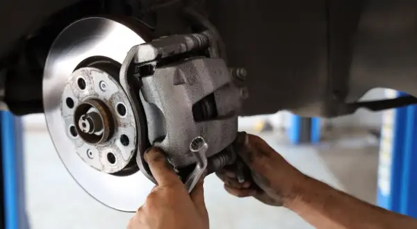 Mechanik dokręca śrubę prowadnicy z gumką góra czy dół, naprawiając hamulce samochodu.