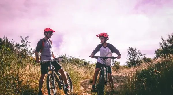 Dwóch rowerzystów w kaskach na tle fioletowego nieba, gotowych do jazdy po malowniczych trasach rowerowych Lublin.