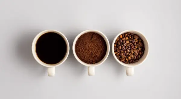 Tre tazze mostrano il viaggio del caffè: chicchi tostati, macinato e bevanda scura. Un'idea di da dove proviene il caffè.