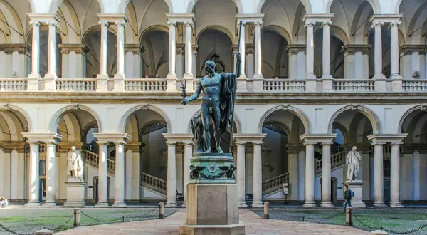 Dziedziniec Pinacoteca di Brera z rzeźbą w centrum i arkadowymi galeriami.