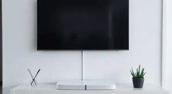 Minimalistyczny salon z telewizorem zamontowanym na ścianie. Pod nim biała szafka z ozdobami i schowkami. Idealna na jakiej wysokości telewizor.