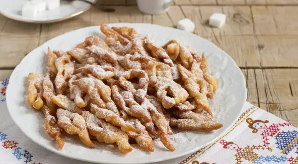 Chrupiące faworki, przepis babci, posypane cukrem pudrem, na talerzu.