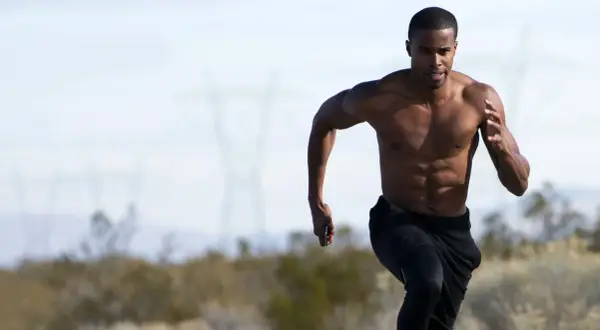 Uomo a torso nudo corre, mostrando i suoi addominali scolpiti. La corsa coinvolge potenti muscoli delle gambe e del core.