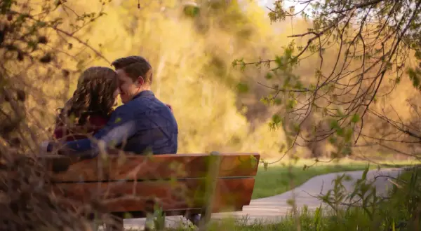 Pareja abrazada en un banco, compartiendo un momento de amor verdadero entre la naturaleza.