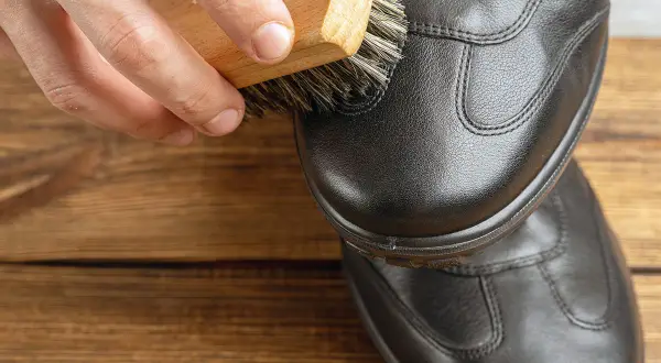 Brosse en bois appliquant un produit sur une chaussure en cuir noir. Pour imperméabiliser chaussures avant ou après cirage, un bon entretien est essentiel.
