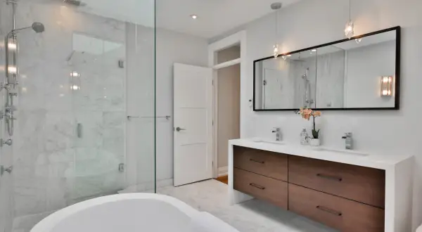 Bagno moderno con vasca freestanding, doccia in cristallo e mobile doppio lavabo con cassetti in legno. Le pareti sono rivestite in marmo, il soffitto è in cartongesso.