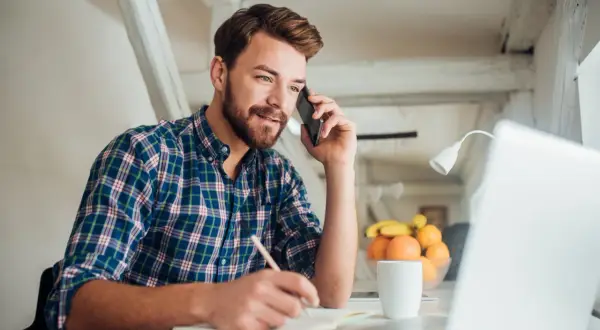 Mężczyzna rozmawia przez telefon, notuje i pracuje przy laptopie. To dobry moment, by zastanowić się, kiedy najlepiej szukać pracy.
