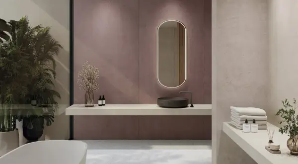 Elegante baño moderno con lavabo de piedra, espejo ovalado iluminado y azulejos de pared en tono malva. Toallas apiladas y plantas aportan calidez.