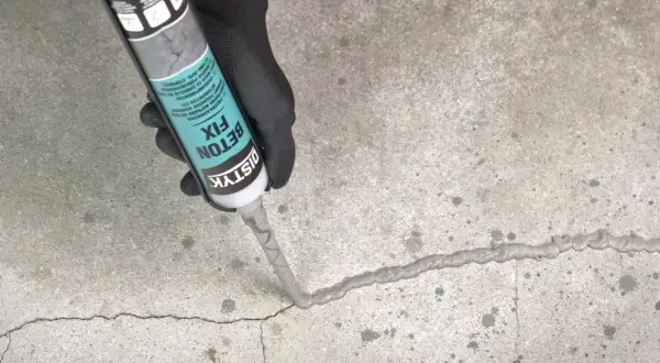 Ręka w czarnej rękawiczce aplikuje masę Distyk Beton Fix na pęknięcie w betonie, pokazując, jak połączyć stary beton z nowym.
