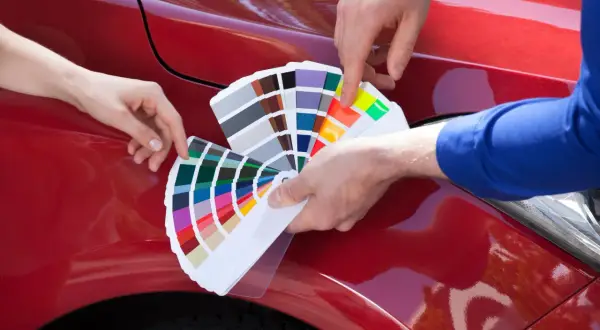 Due mani scelgono la vernice auto che cambia colore, confrontando campioni su un'auto rossa lucida.