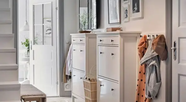 Elegante decoración de entradas y recibidores: zapateros blancos, perchero con abrigos y un banco de madera invitan a entrar.
