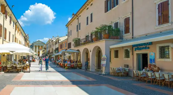 Passeggiata nel bardolino centro storico, con tavolini all'aperto e gente che gode del sole.